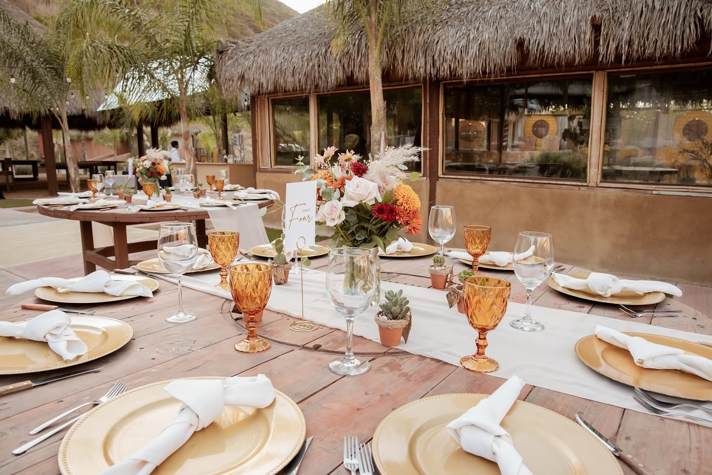 Mesa montada con vajilla dorada y centro de flores en la terraza